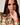 A Model wearing the Liquid in Coral patent leather Apple watch band by Chalonne with a peach blouse with a sage and coral interlocking chain pattern